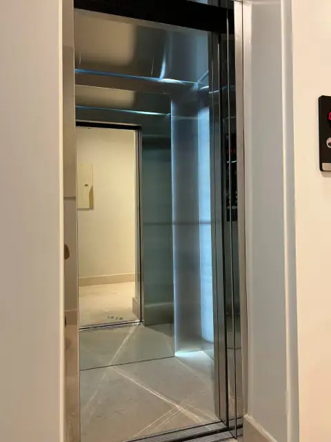 Open glass-door cabin, stainless door frame and call button on cream wall