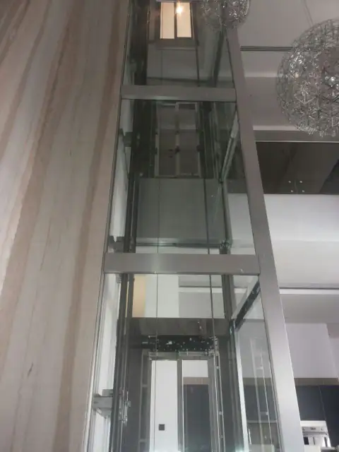 Tall glass shaft beside a chandelier in a double-height space