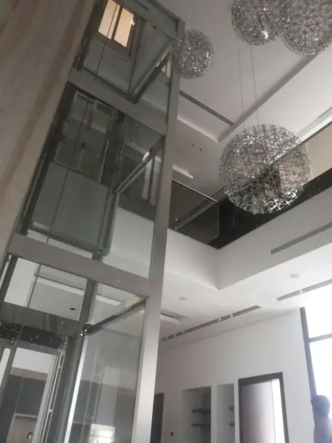 Glass panoramic lift shaft rising through a double-height lounge